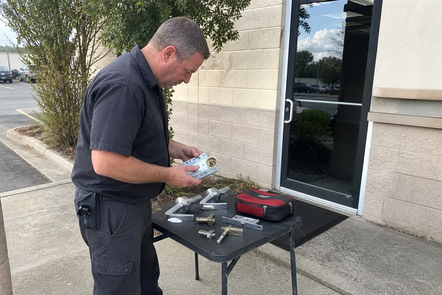 Technician examining detached commercial lock hardware on a table outside a shop entrance. — Business Lockout Service, Port Colborne