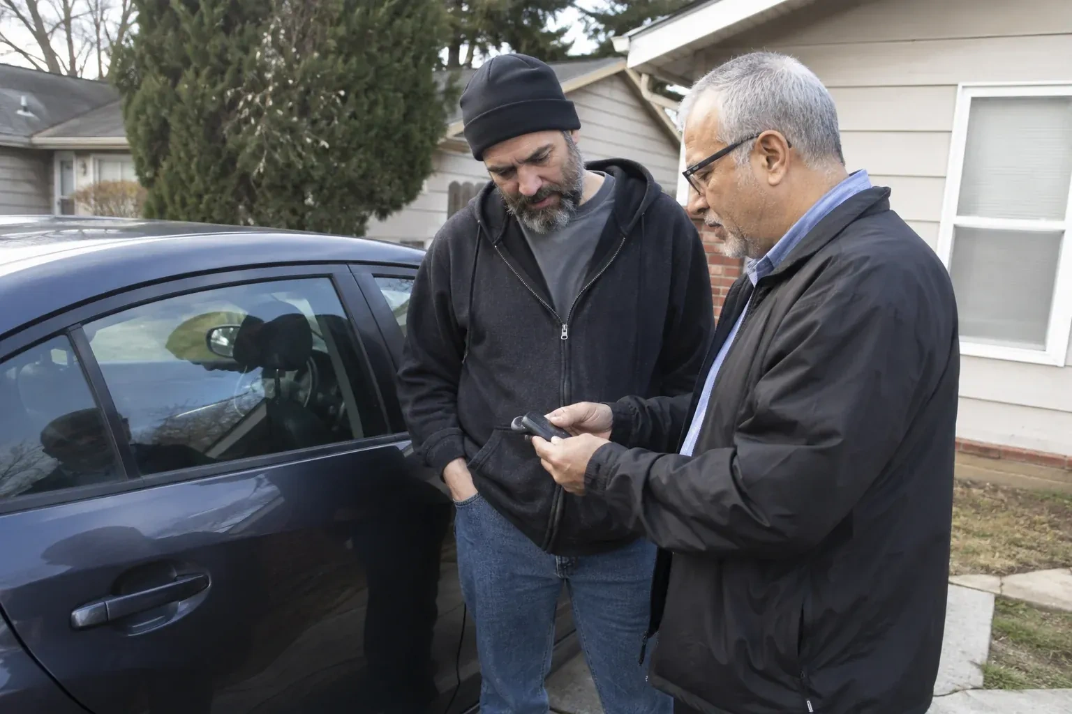 Two adults discussing a key fob beside a parked car. — Car Lockout Service, Port Colborne