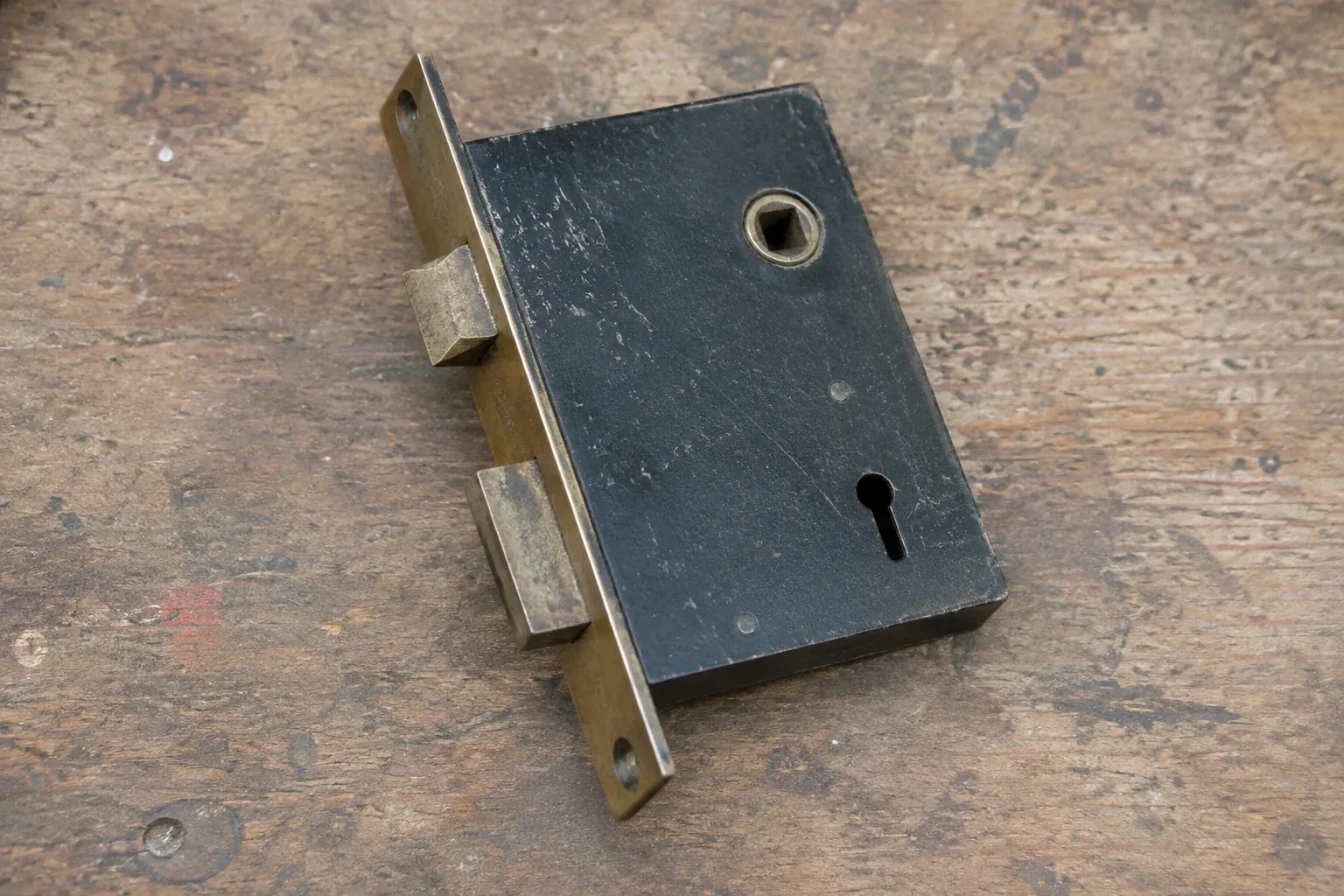 Closed mortise lock case with spindle opening, keyhole, latch and deadbolt on a wooden workbench. — Vintage Mortise Lock Service, Port Colborne
