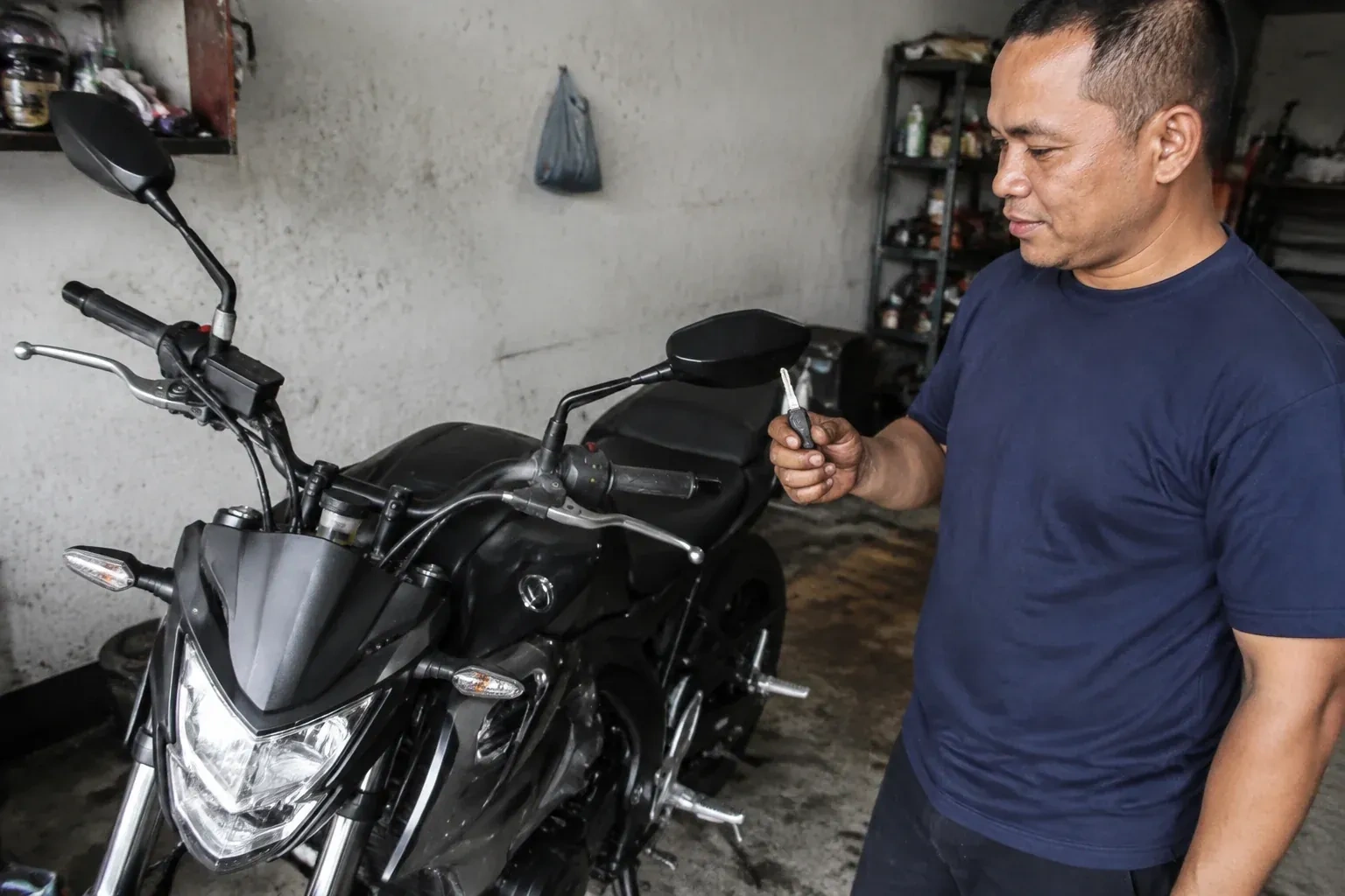 Person holding a key beside a black motorcycle in a garage. — Motorcycle & Scooter Keys, Port Colborne